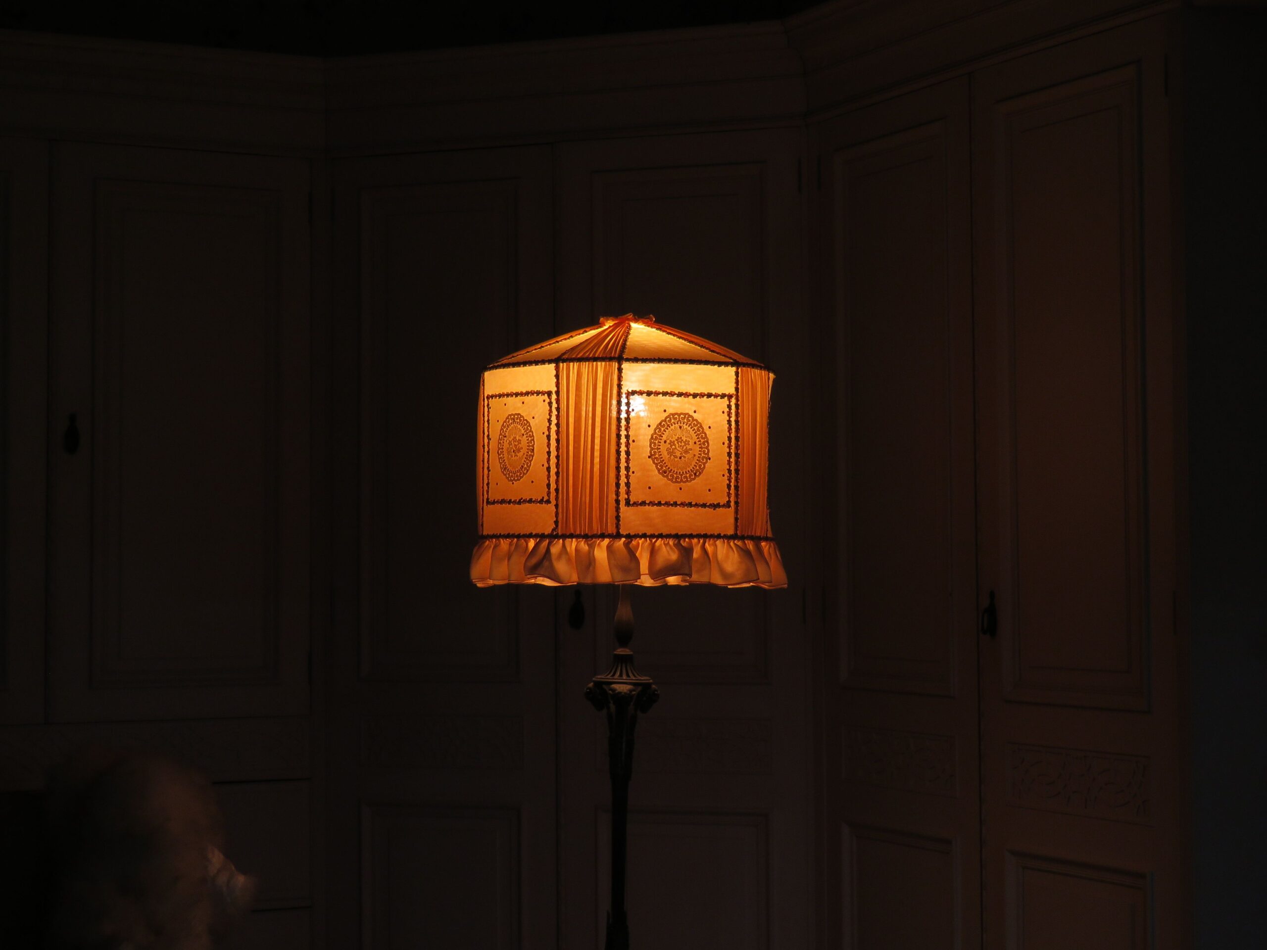 Textured pleated linen lampshade casting warm decorative shadow pattern on wall in cozy living room corner