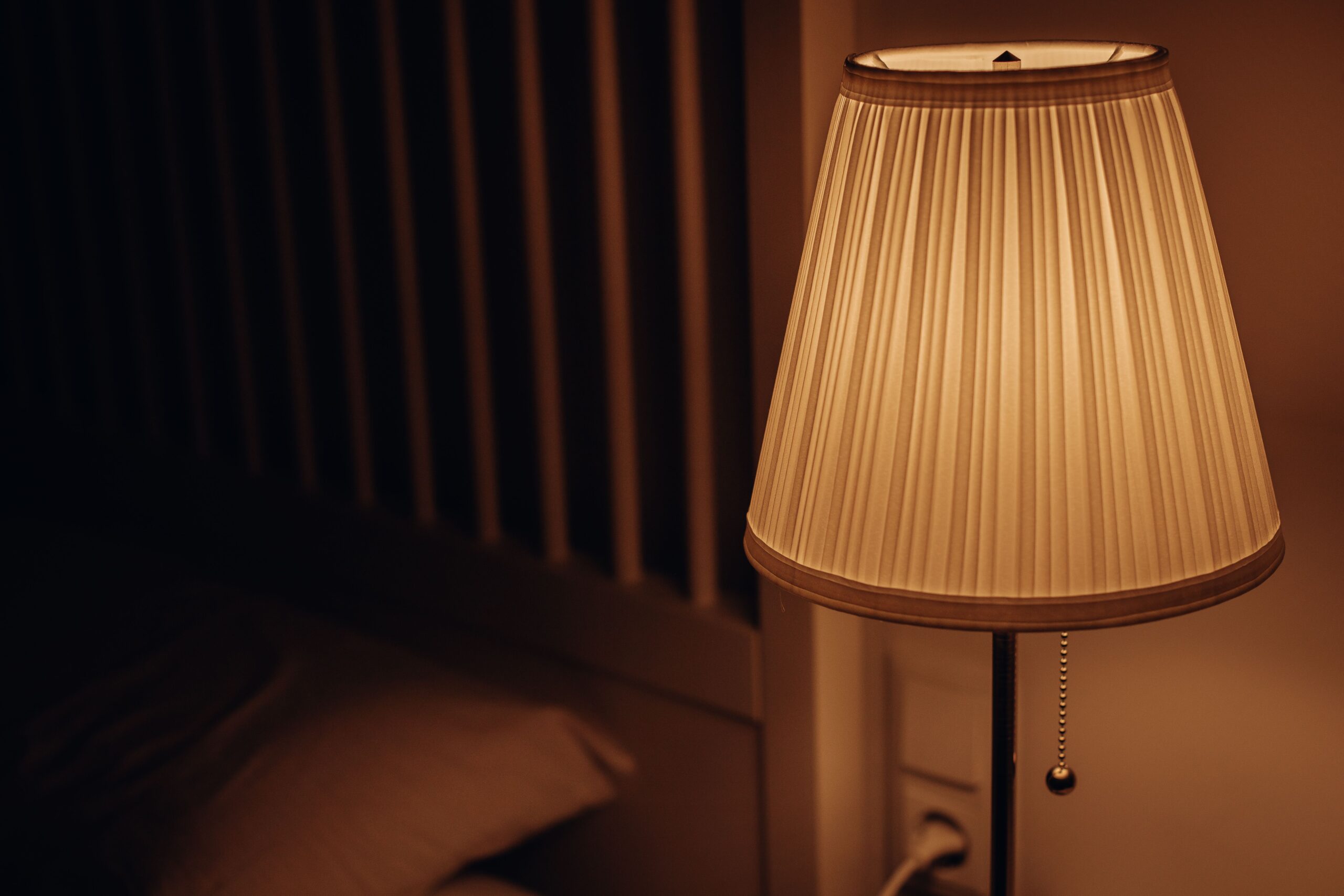 Close up of warm 2700K soft white bulb glowing amber inside textured lampshade on wooden side table